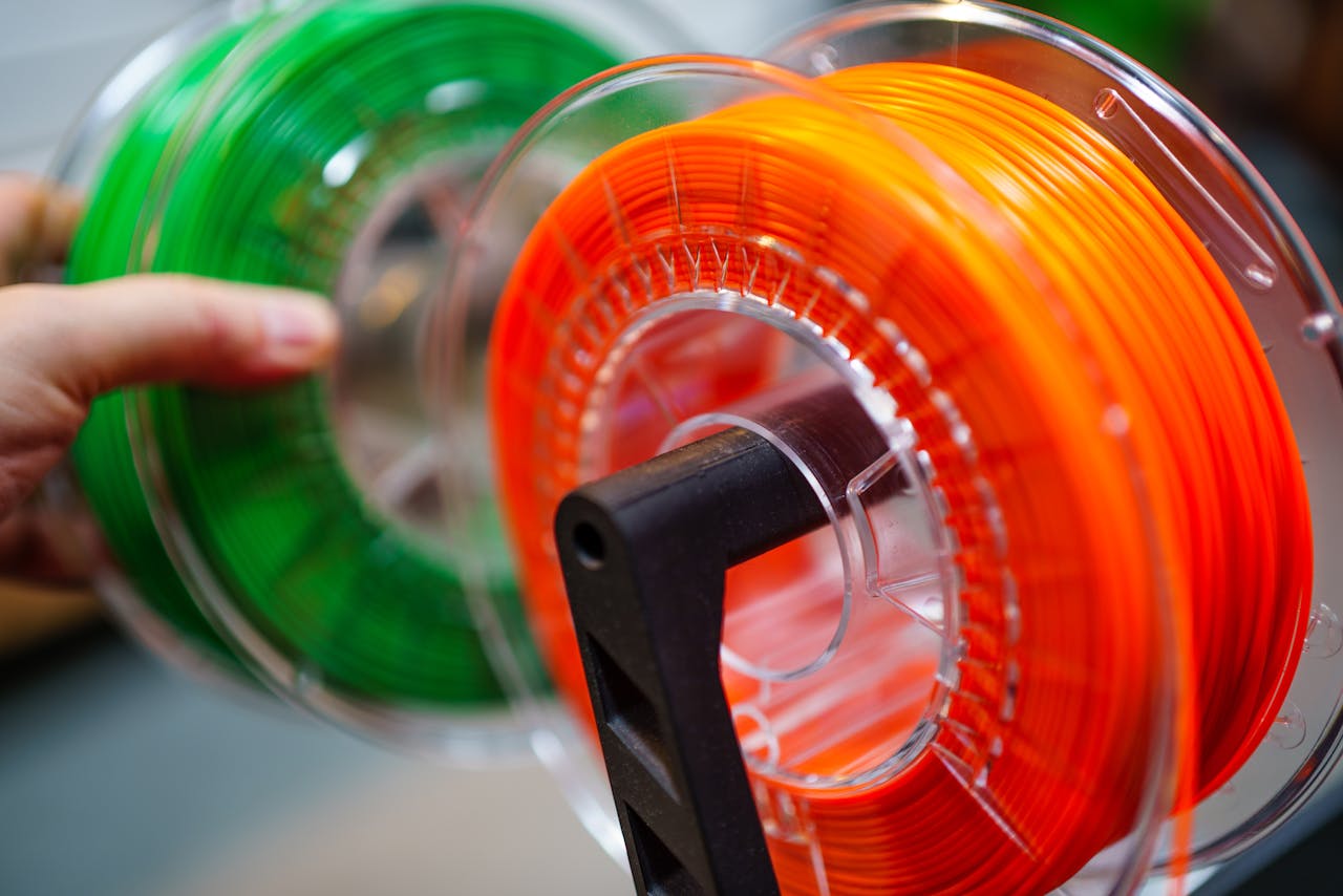 Vibrant orange and green 3D printer filament spools for innovative manufacturing uses.